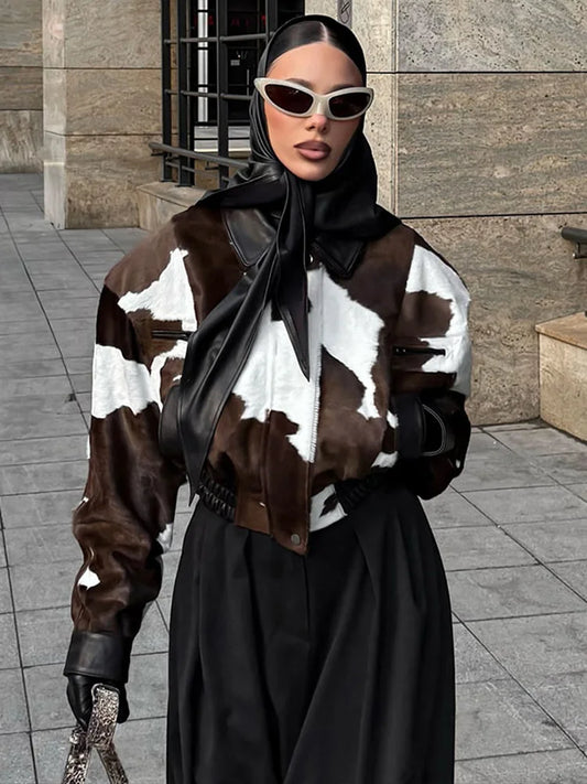 Person wearing a cow print jacket and black outfit with sunglasses in an urban setting