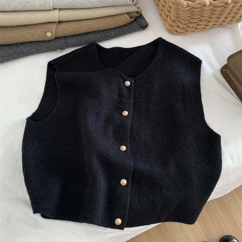 Black vest with button details on a white surface with folded clothes in the background