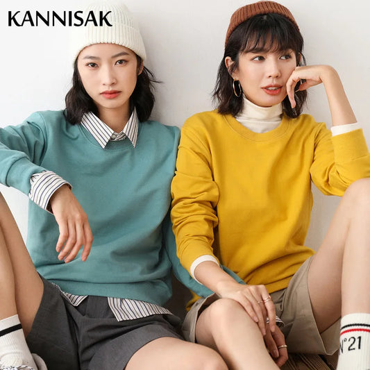 Two women sitting side by side wearing colorful sweaters with 'KANNISAK' branding.