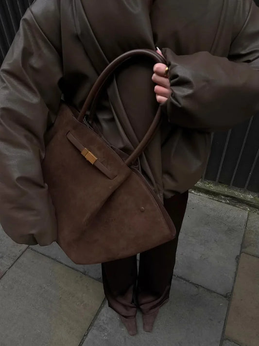 Person wearing a brown coat holding a matching brown bag on a sidewalk.