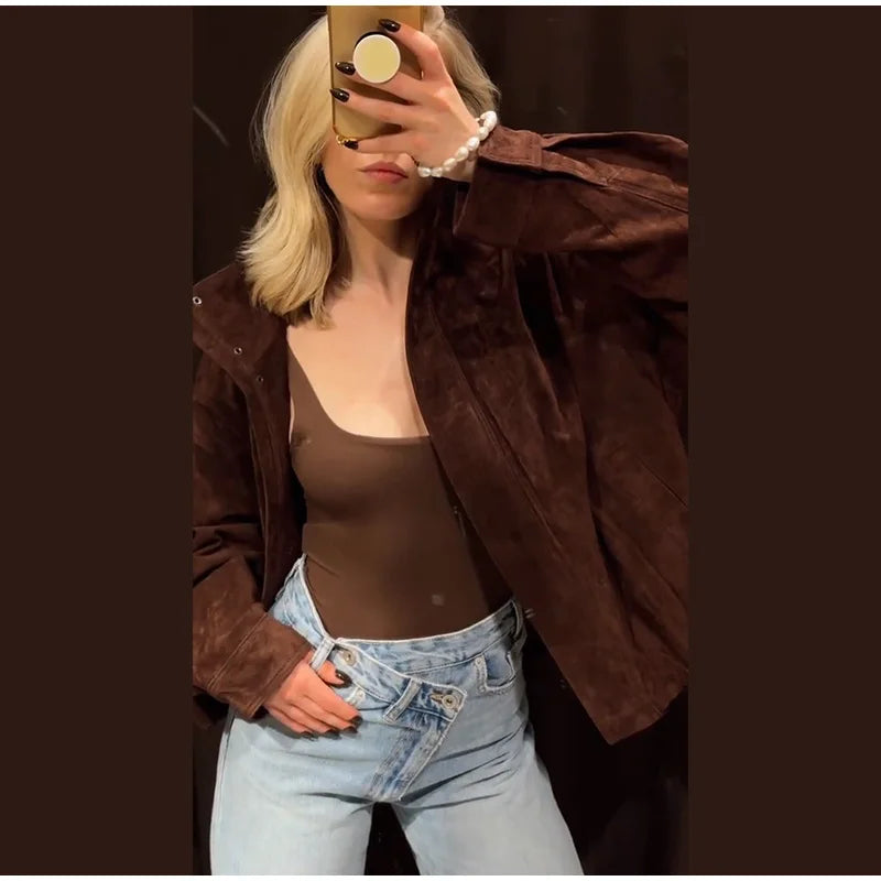 Person wearing a brown jacket and jeans taking a mirror selfie.