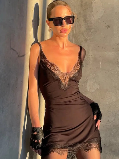 Woman wearing a brown lace dress and sunglasses against a gray wall.