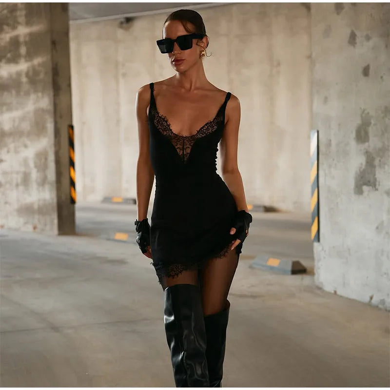 Woman in a black lace dress and knee-high boots standing in an industrial setting.