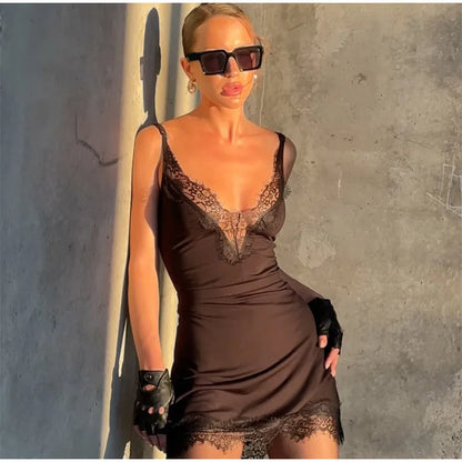 Woman wearing a brown lace dress against a concrete wall.