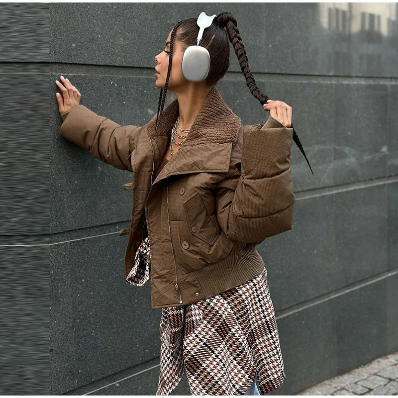 Person wearing a brown jacket and plaid pants against a dark wall.