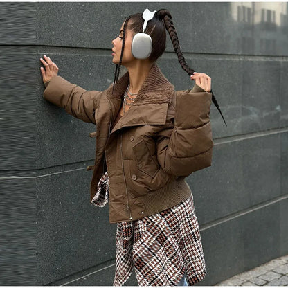 Person wearing a brown jacket and plaid pants against a dark wall.