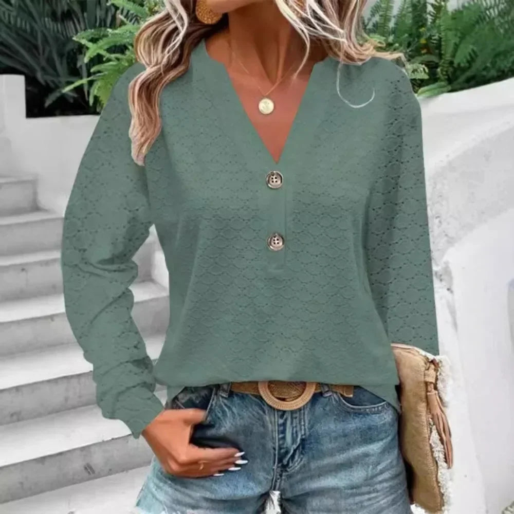 Person wearing a green textured sweater with buttons and blue jeans outdoors.