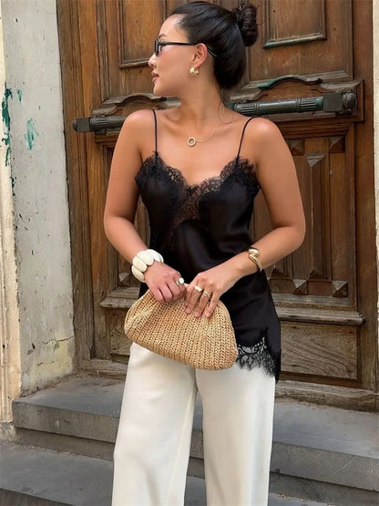 Woman in black lace top and white pants holding a straw bag, standing in front of a wooden door.