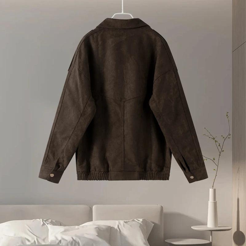 Brown jacket hanging on a gray wall with a bed and vase in the foreground