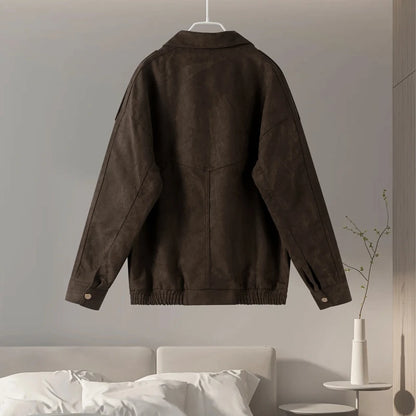 Brown jacket hanging on a gray wall with a bed and vase in the foreground