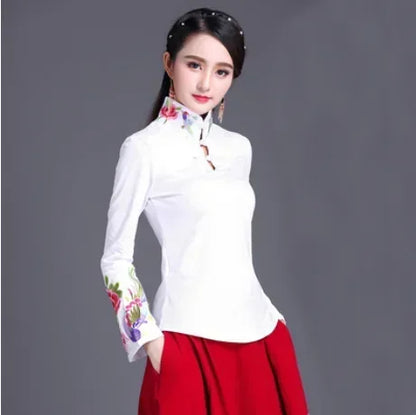 Woman wearing a white blouse with floral embroidery and a red skirt on a gray background