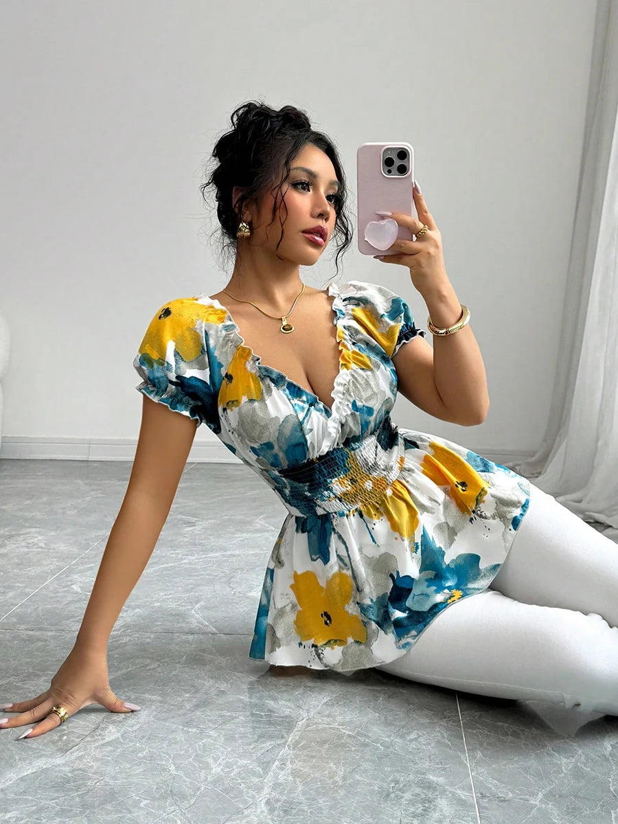 Woman taking a selfie in a floral dress and white pants on a gray floor.