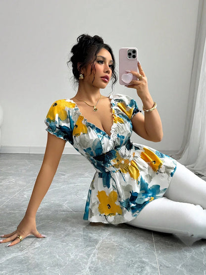 Woman taking a selfie in a floral dress and white pants on a gray floor.