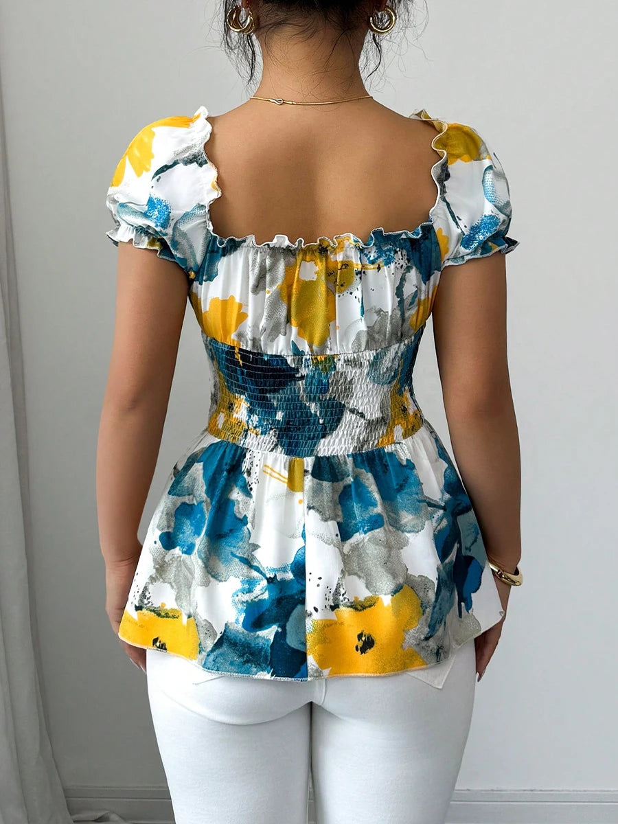 Woman wearing a colorful floral top with ruffled sleeves against a plain background