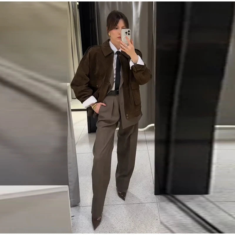 Person wearing a brown jacket and gray pants taking a mirror selfie.