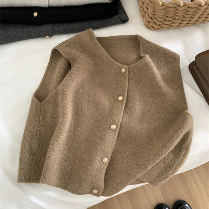 Brown cardigan on a white surface with folded clothes in the background