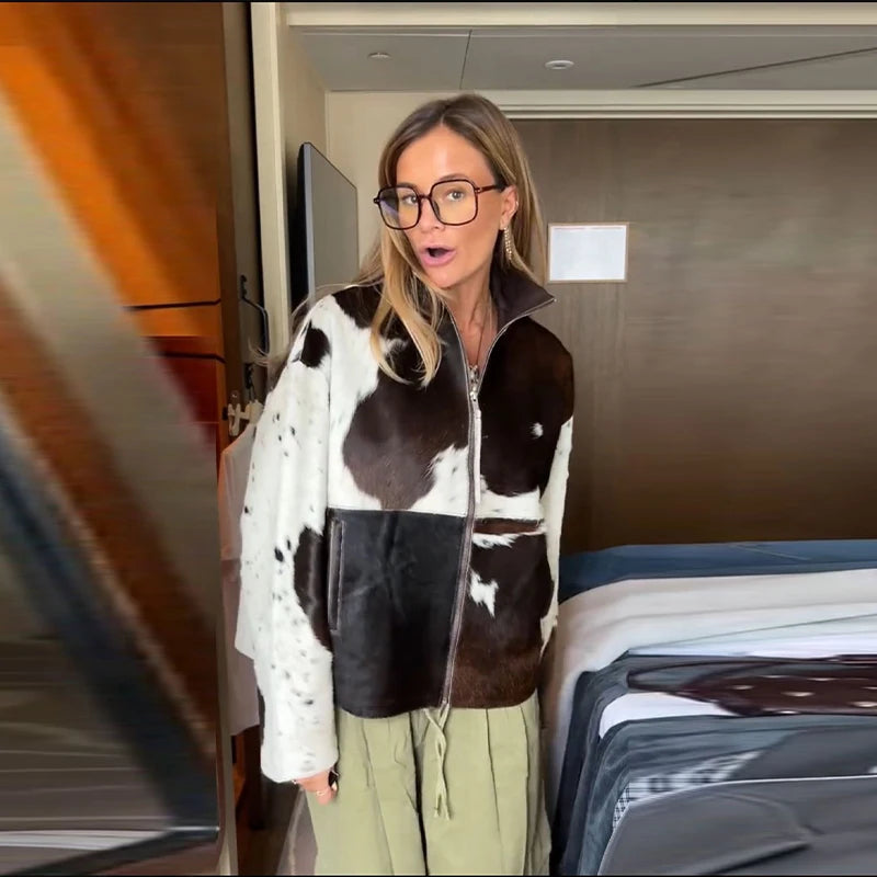 Woman wearing a cow print jacket in a room with a bed and wardrobe.
