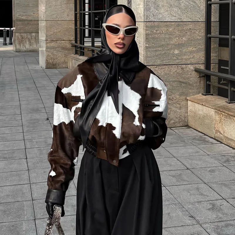 Person wearing a cow print jacket and black coat on a city street.