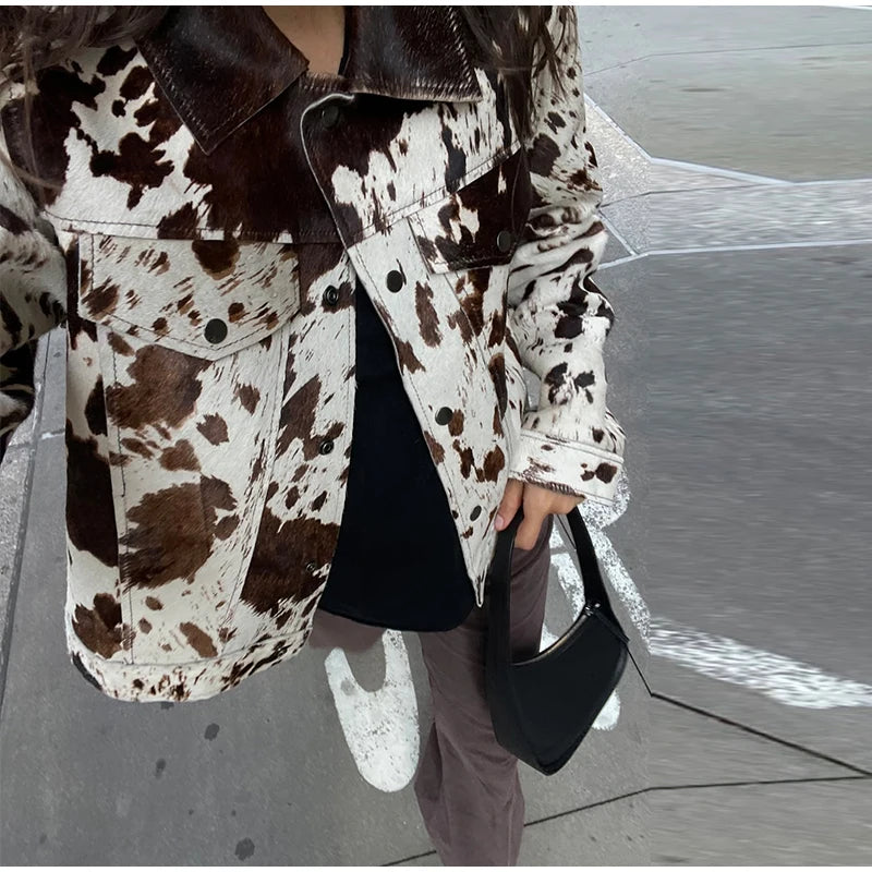 Person wearing a cow print jacket on a beach.