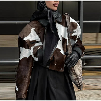 Person wearing a cow print jacket with a black scarf and gloves in an urban setting.