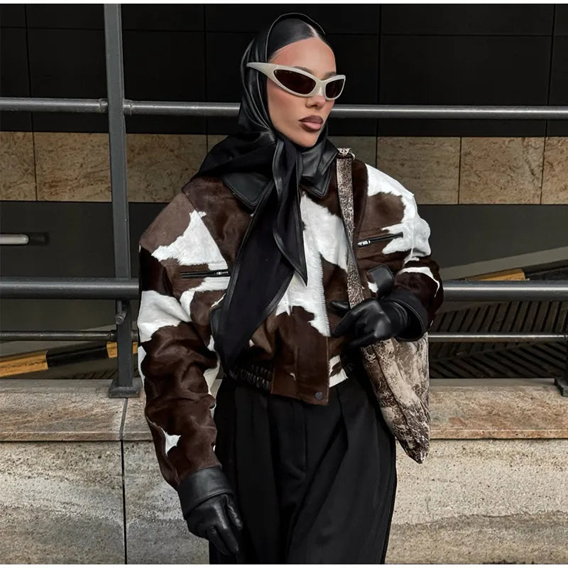 Person wearing a cow print jacket with a black scarf and sunglasses in an urban setting.