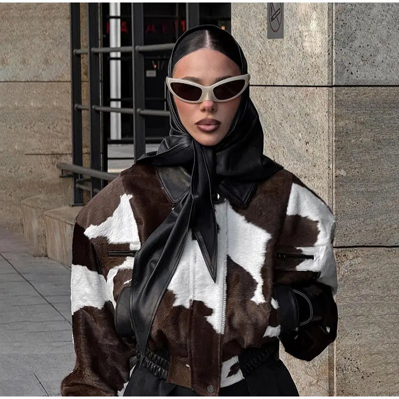 Person wearing a cow print jacket with a scarf, standing against a building exterior.