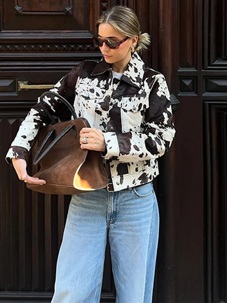 Person wearing a cow print jacket and holding a brown bag against a dark wooden background