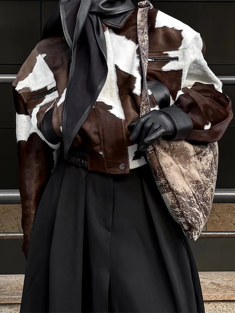 Person wearing a cowhide leather jacket with a patterned design, holding a matching bag.