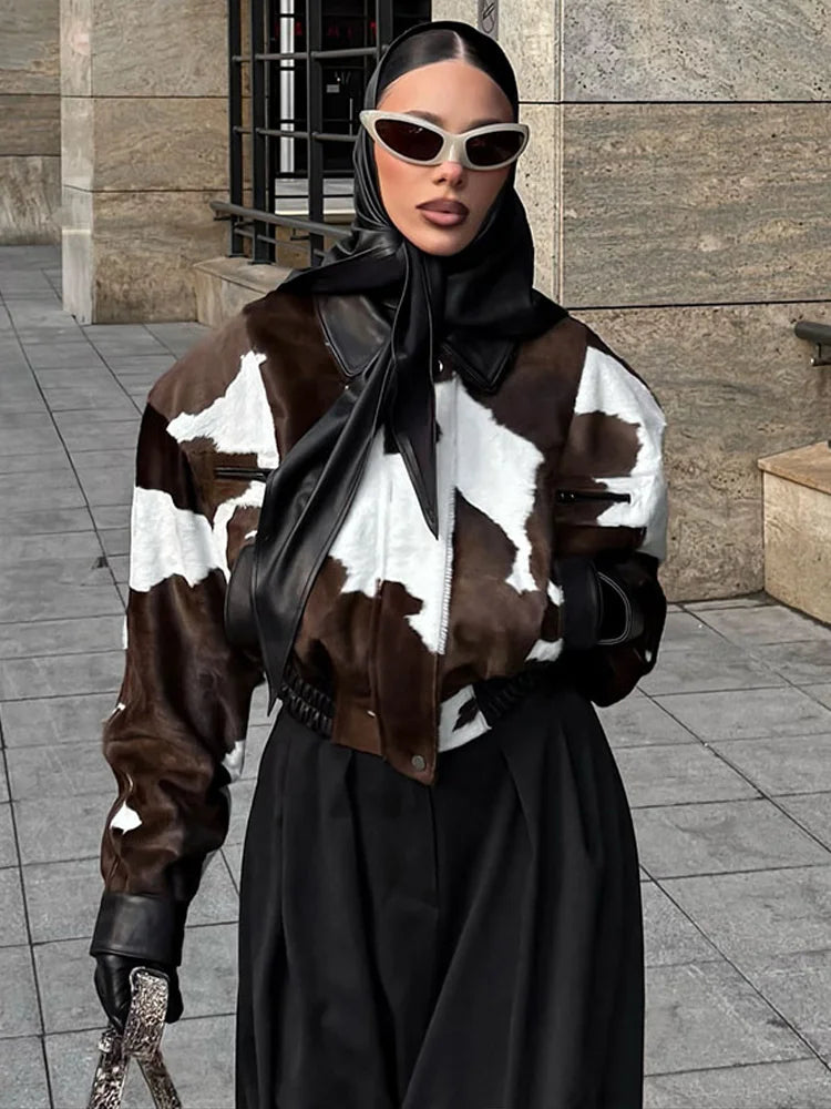Person wearing a cow print jacket and black outfit with sunglasses in an urban setting