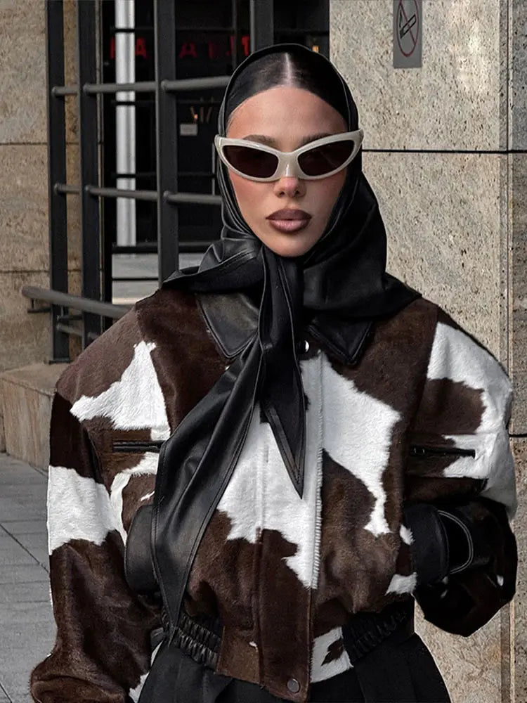Person wearing a cow print coat with a black scarf and sunglasses in an urban setting