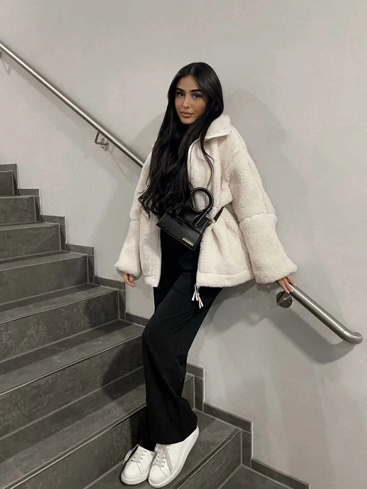 Woman in a white coat sitting on a staircase holding a black handbag.