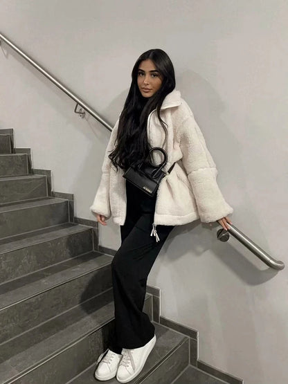 Woman in a white coat sitting on a staircase holding a black handbag.