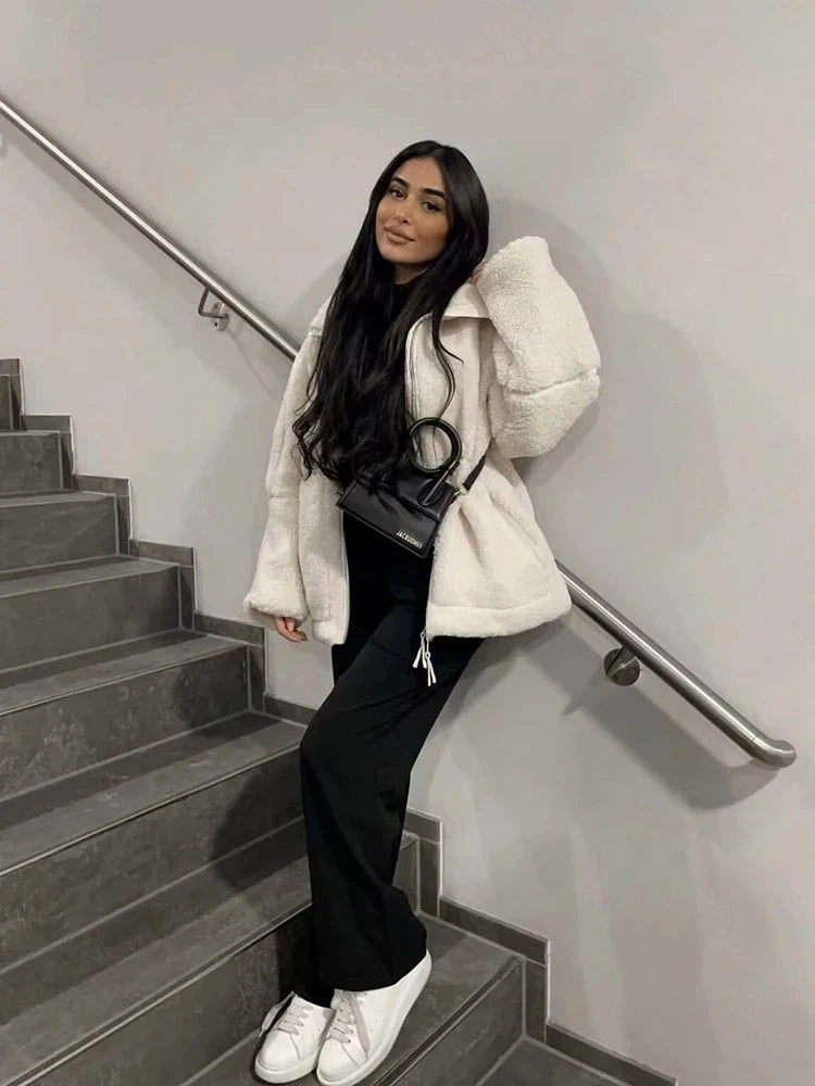 Person wearing a white coat, black pants, and white sneakers on a staircase.