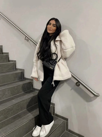 Person wearing a white coat, black pants, and white sneakers on a staircase.