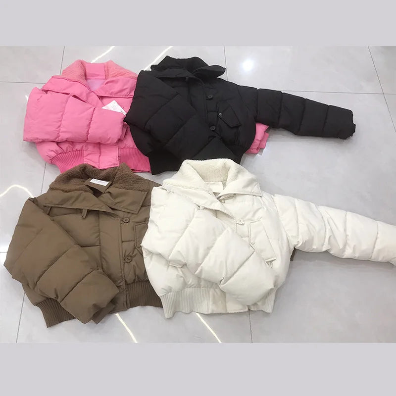 Four puffer jackets in pink, black, brown, and white on a light gray floor.