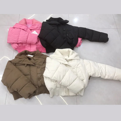 Four puffer jackets in pink, black, brown, and white on a light gray floor.