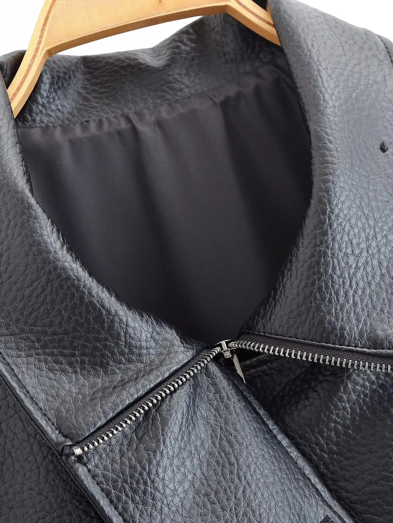 Close-up of a black leather jacket with a zipper on a wooden hanger.