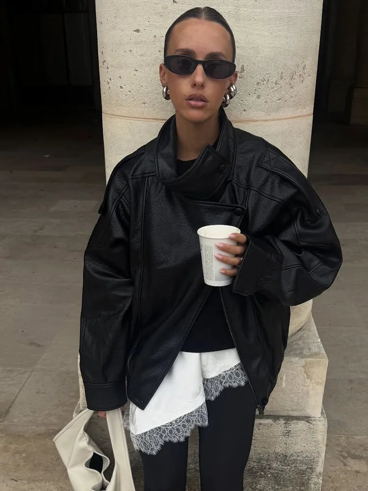 Person wearing a black jacket and sunglasses, holding a white cup against a neutral background