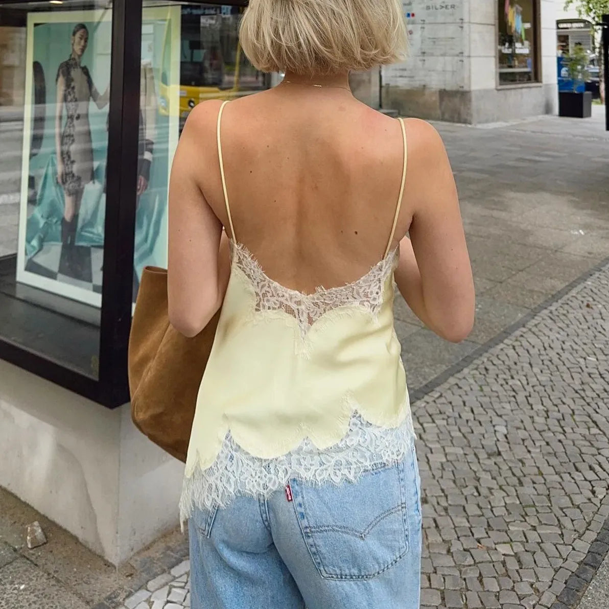 Woman wearing a yellow lace top and blue jeans walking on a street.