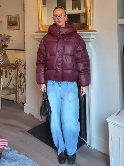 Person wearing a maroon puffer jacket and light blue jeans indoors.