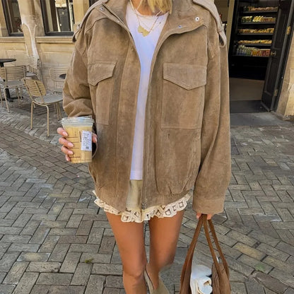 Person wearing a brown suede jacket holding a coffee cup on a sidewalk.