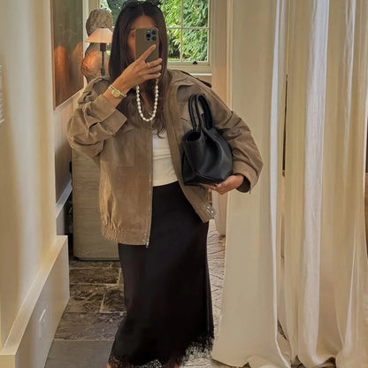Person taking a mirror selfie wearing a brown jacket, white top, black skirt, and holding a black handbag.