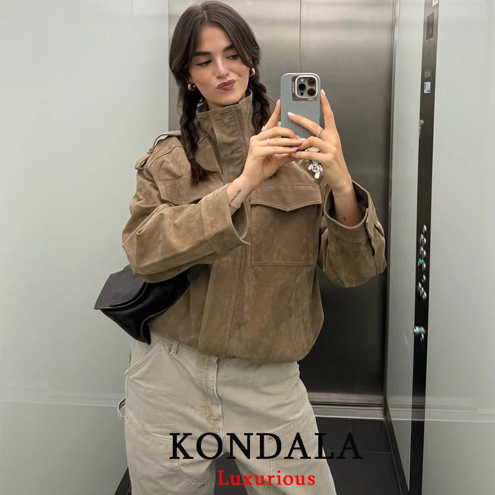Person taking a mirror selfie wearing a brown jacket and beige pants in an elevator, with 'KONDALA Luxurious' branding.