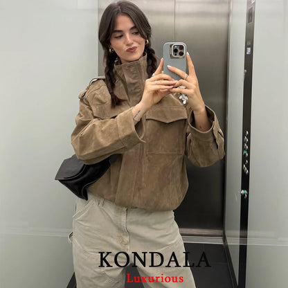 Person taking a mirror selfie wearing a brown jacket and beige pants in an elevator, with 'KONDALA Luxurious' branding.