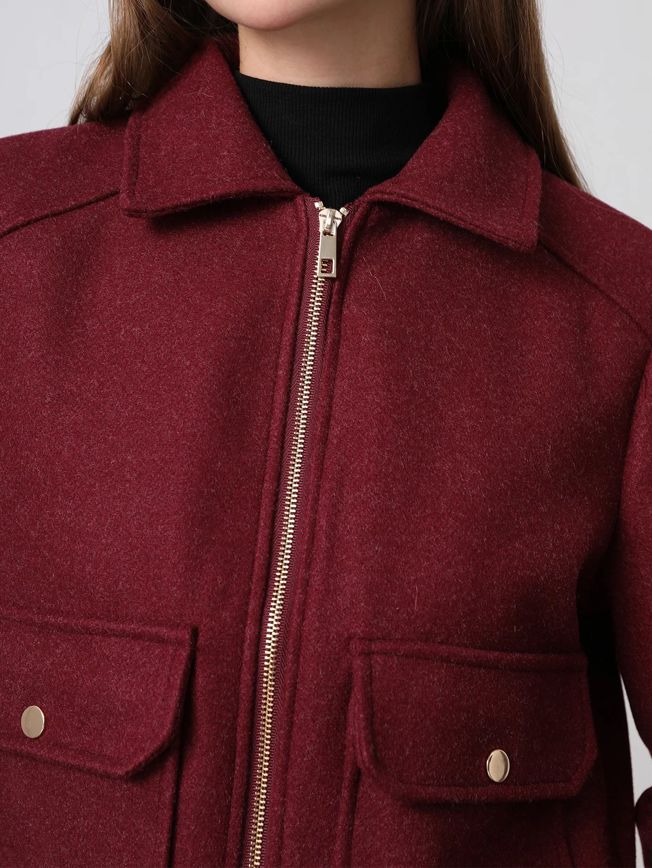 Close-up of a maroon jacket with a zipper and button details on a plain background