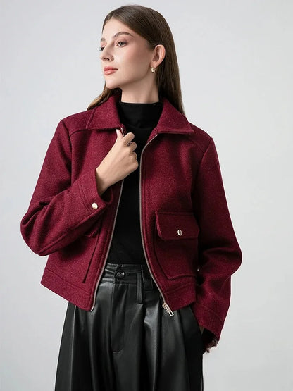 Woman wearing a burgundy jacket over a black top and skirt on a light gray background
