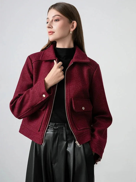Woman wearing a burgundy jacket over a black top and skirt on a light gray background