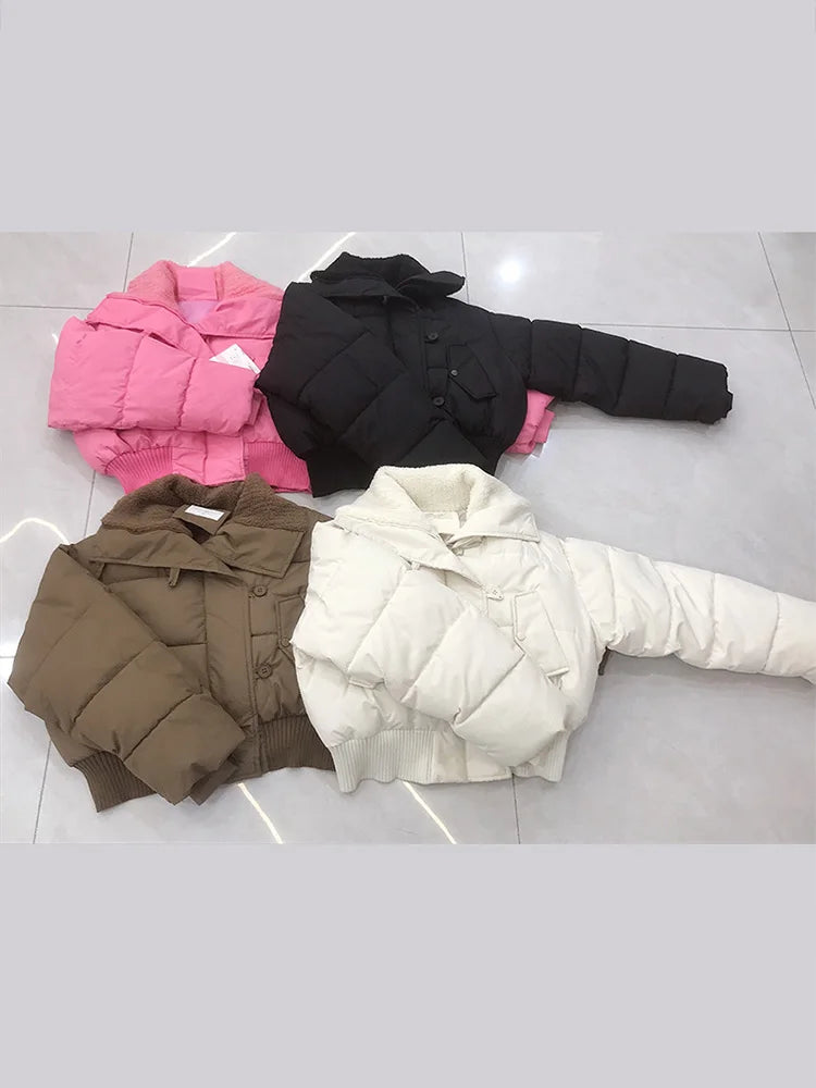 Four puffer jackets in pink, black, brown, and white on a light gray floor.