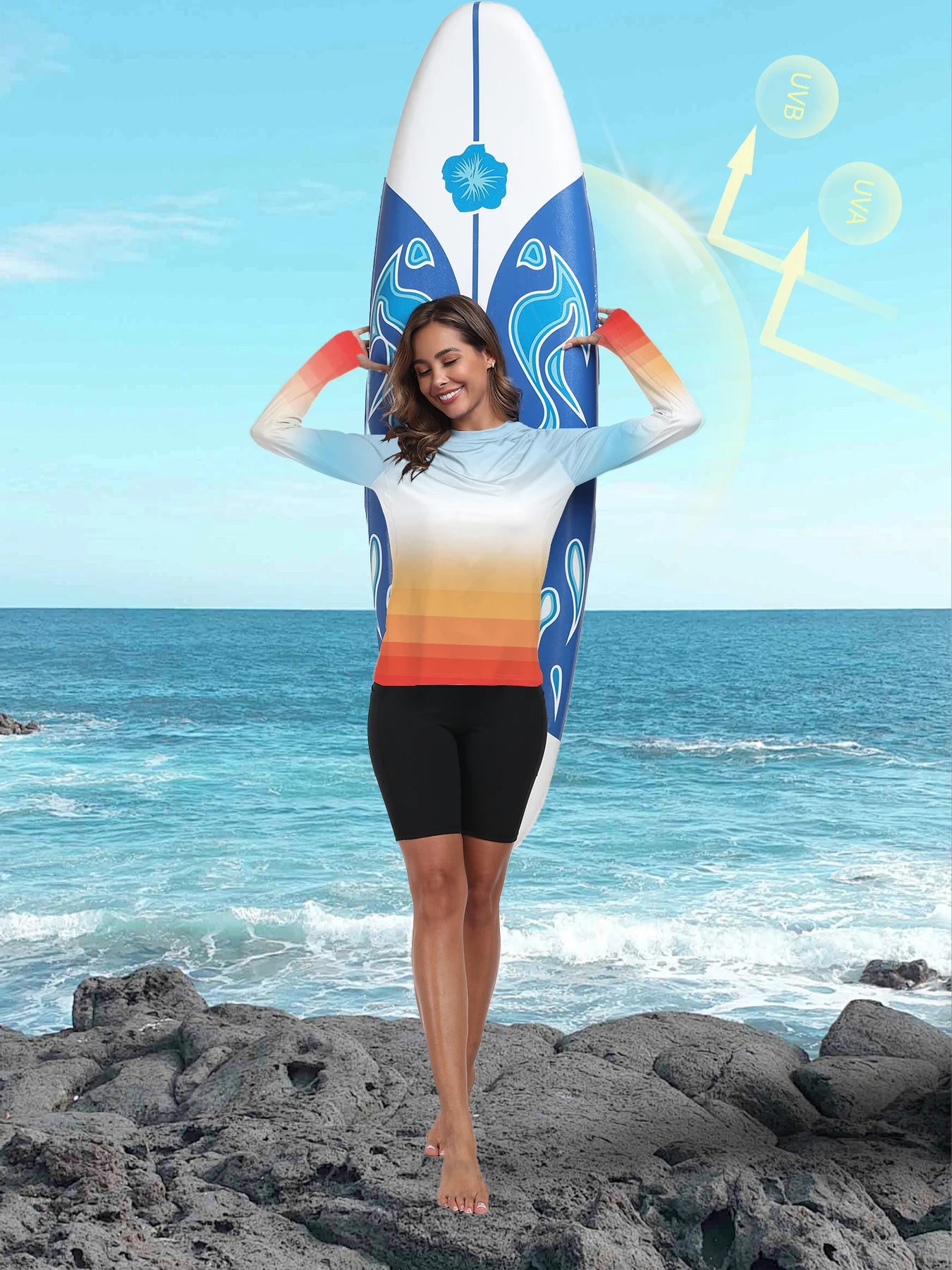 Woman in a gradient swimsuit standing on rocks with a surfboard in the background
