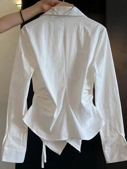 White blouse with a unique design held up on a hanger against a dark background